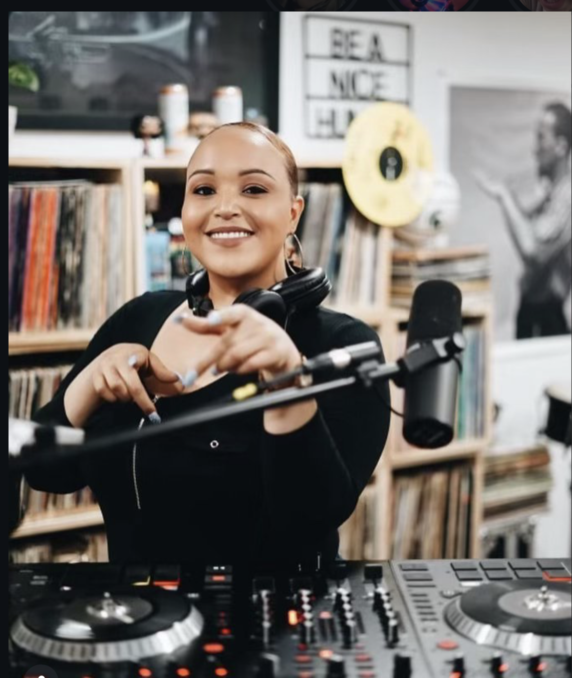 DJ Lala Land at the DJ decks, wearing headphones, with a microphone and record collection